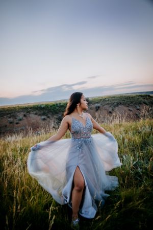 Flowing blue gown twirls dramatically in golden field during sunset photoshoot.
