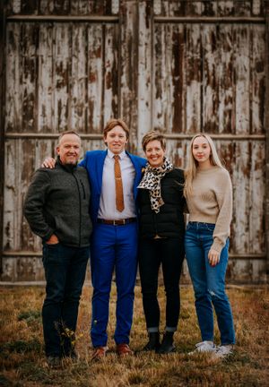Casual family portrait with four people standing against rustic barn wall.