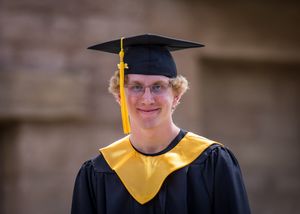 Graduate wearing academic regalia with black cap and yellow stole at graduation ceremony.