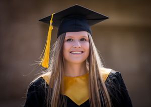Graduate wearing traditional black graduation cap and gown with yellow stole and tassel.