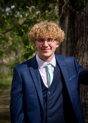 Person in navy blue three-piece suit with mint green tie outdoors.