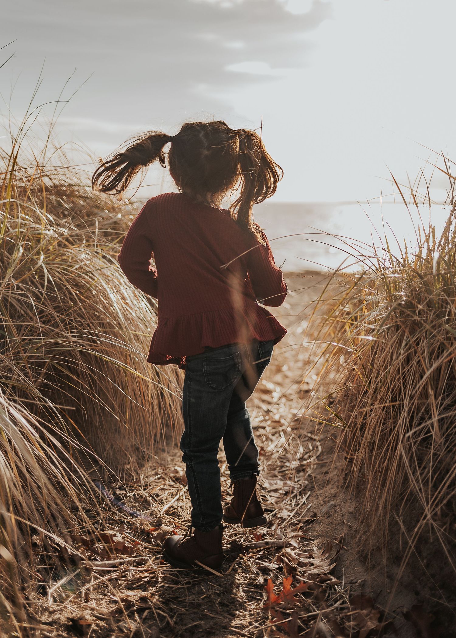 A young girlis dancing through tall grass along a coastal path at sunset in East Providence/Rumford, Rhode Island.