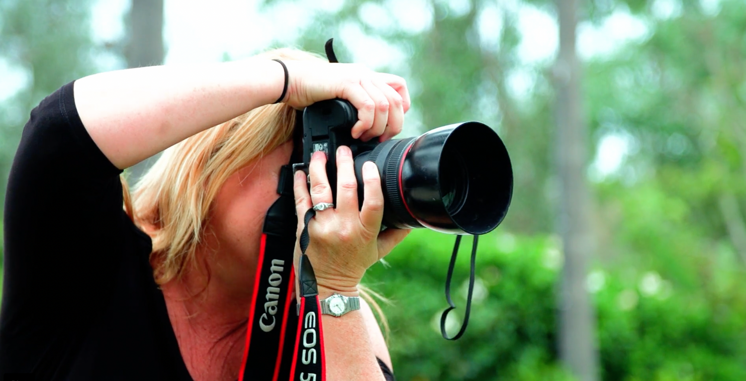 Woman photographing with professional Canon camera and telephoto lens outdoors.