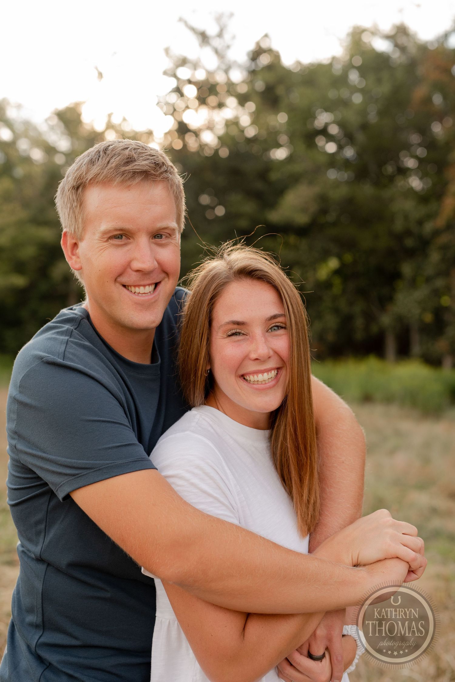 A joyful embrace captured in warm evening light with trees and meadow in the background.
