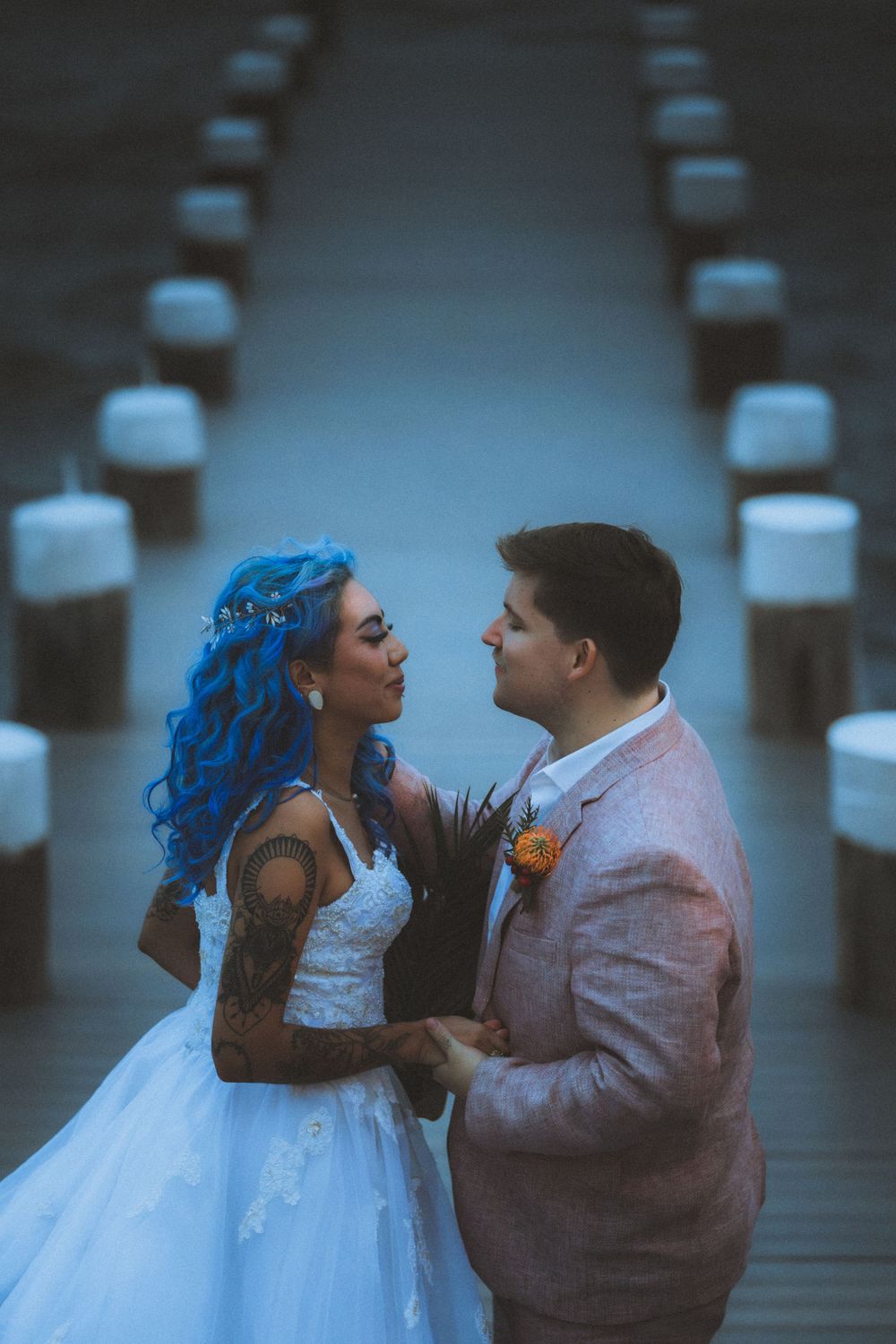 A romantic wedding photo on a boardwalk with blue-haired bride in white dress and groom in pink suit.
