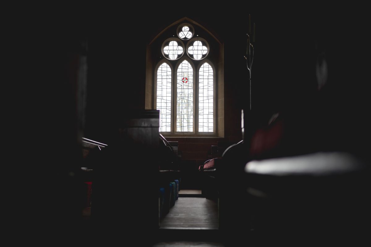 Dark church interior with sunlight streaming through a Gothic stained glass window.