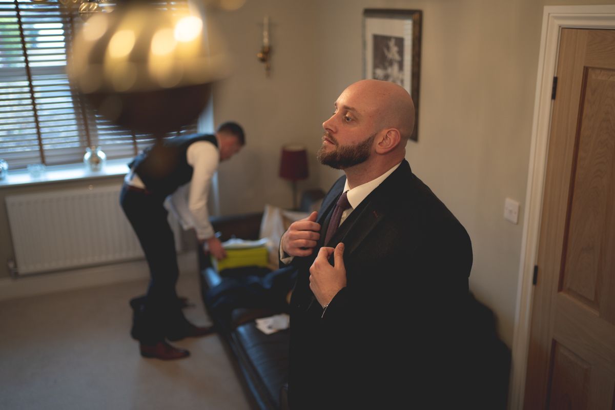 Two people in formal attire preparing in a room with casual lighting.