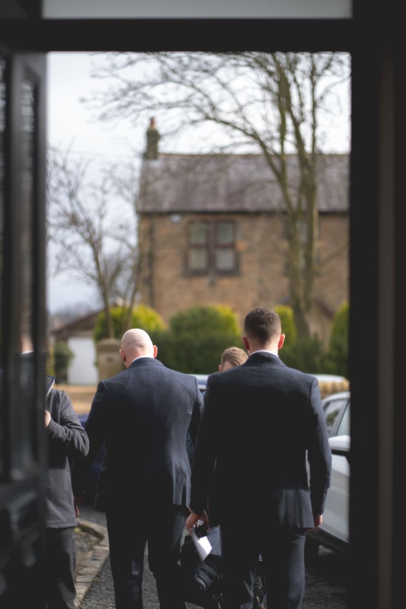 Men in suits walking outside a stone building on an overcast day.