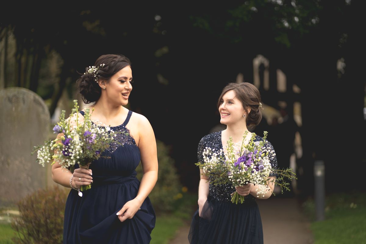 Two bridesmaids in navy dresses hold colorful bouquets while standing outdoors.
