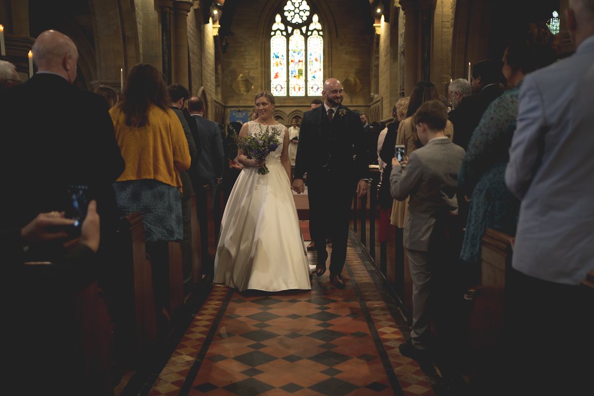 Newlyweds walk down the aisle as guests look on in a traditional church ceremony.