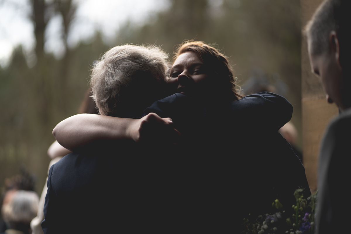 Two figures embrace in an emotional moment at an outdoor gathering.