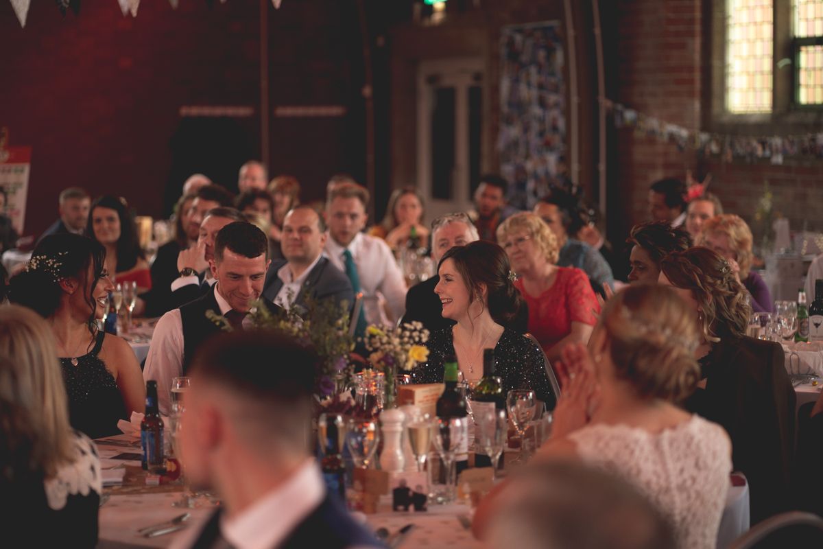 Wedding reception guests seated at decorated tables engage in conversation.
