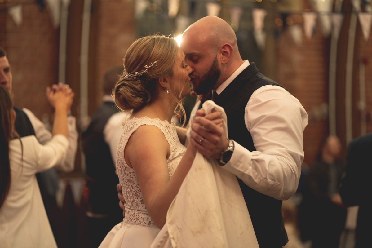 A couple dances closely together during their wedding reception under festive string lights.
