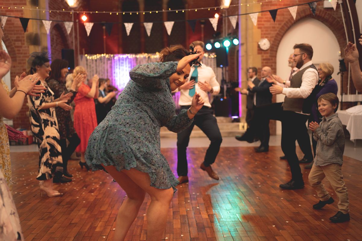 Wedding guests dancing energetically on a wooden dance floor decorated with colorful bunting.