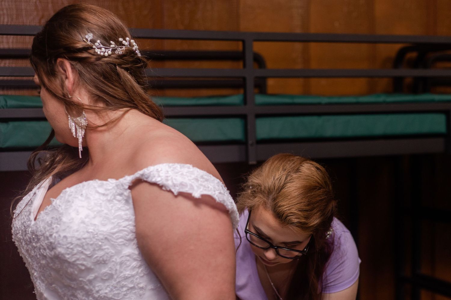 Wedding party members assist with the bride's dress details in a reception hall.