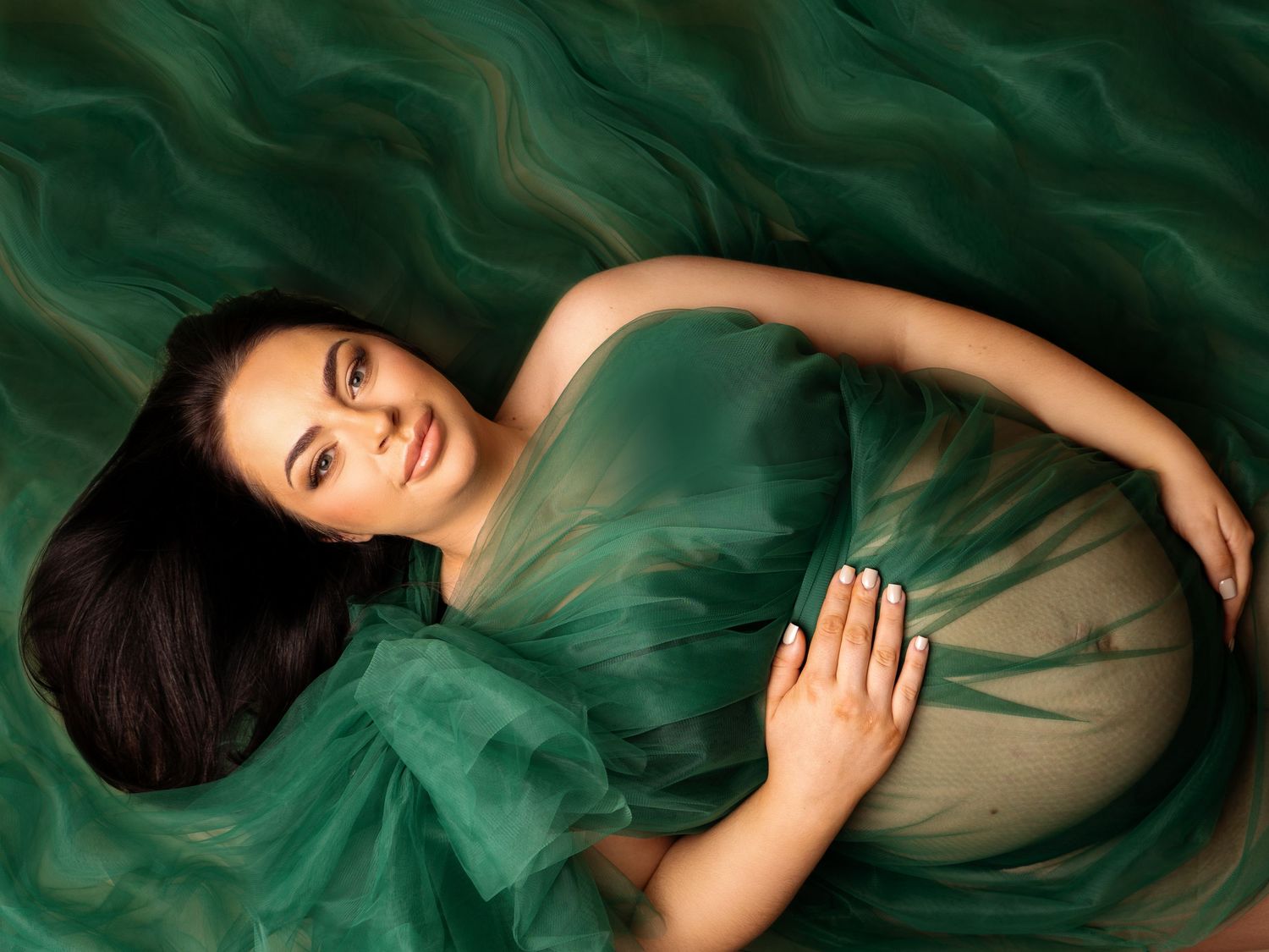 pregnant lady laid on green fabric luxury dress, holding bump with newborn photographer in doncaster.