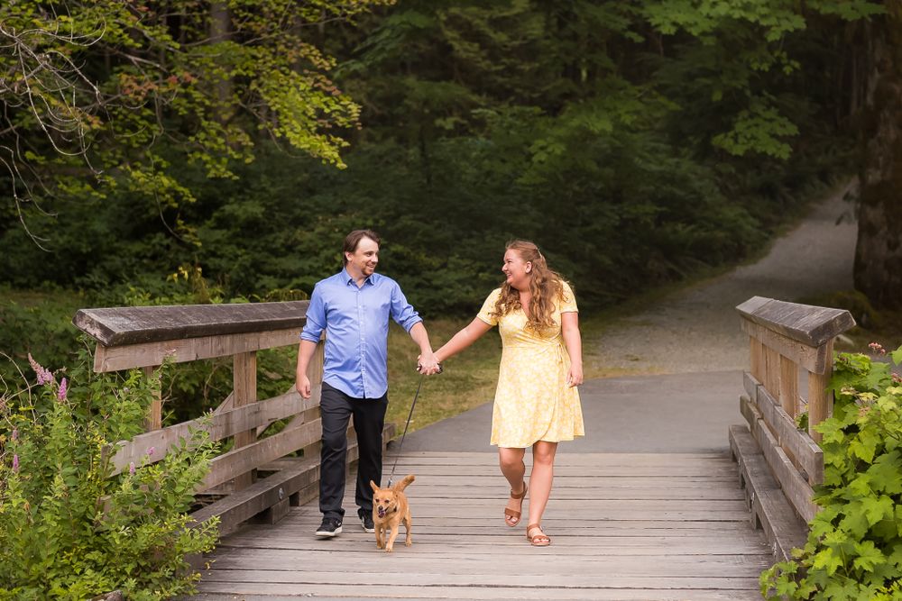 A couple dressed nicely hold hands and walk together along a small wooden bridge.