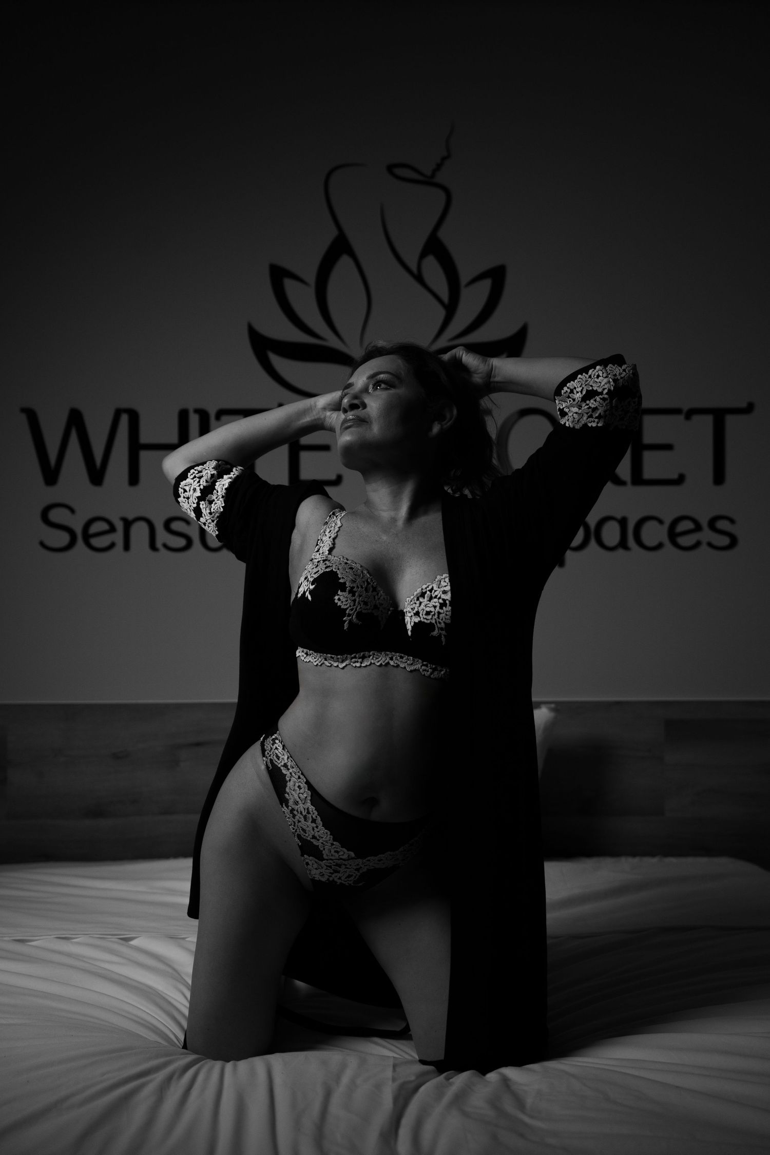 Intimate monochrome portrait with soft lighting against white bedding.
