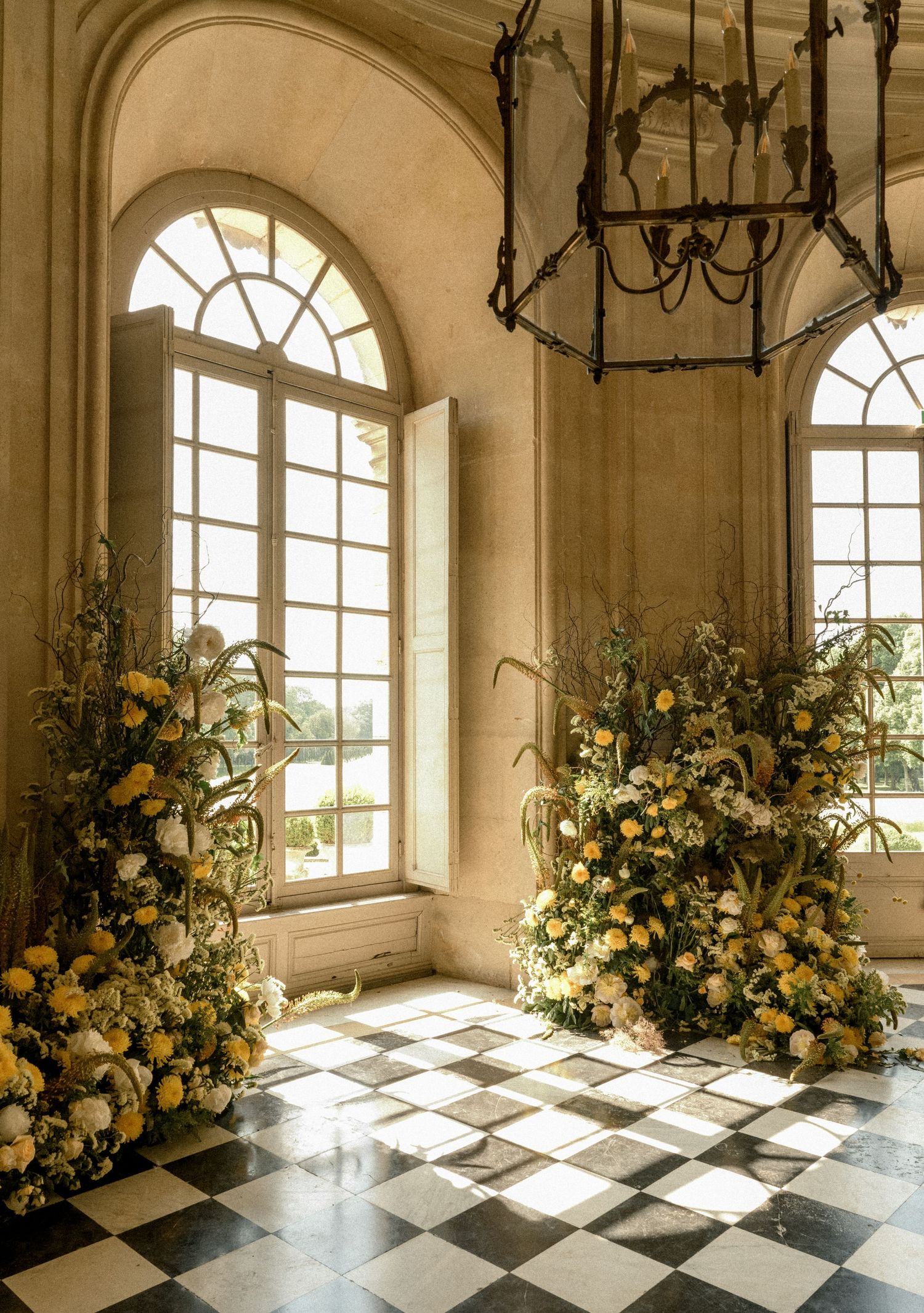 Elegant room interior with checkerboard floor, arched windows and yellow floral arrangements.