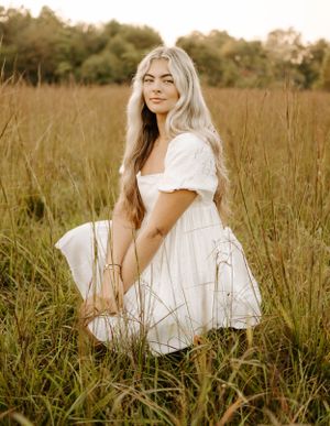 White summer dress flows gracefully amidst tall grass in warm evening light.