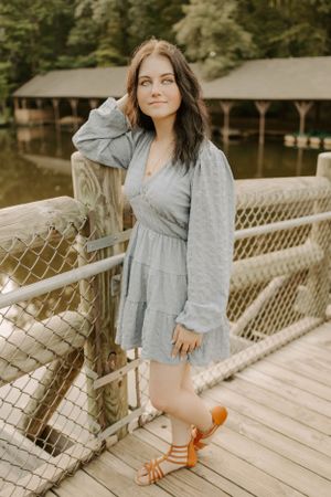 Portrait on wooden bridge overlooking boathouse in grey summer dress.