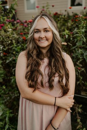 Portrait of woman in pink dress standing in front of blooming rose garden.