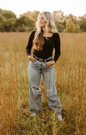 Casual style portrait in ripped jeans and black top standing in autumn field.