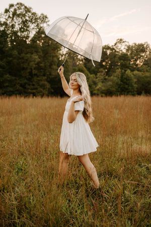 Playful pose with transparent umbrella in tall grass during golden hour.