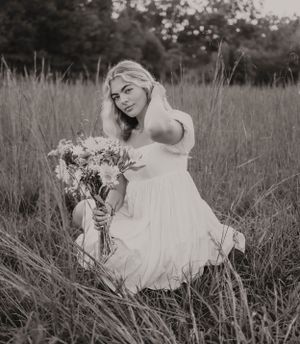Black and white portrait with flowing white dress and wildflower bouquet in meadow setting.