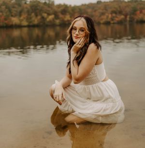 Dreamy portrait in a white dress by the water with autumn foliage reflected in the background.
