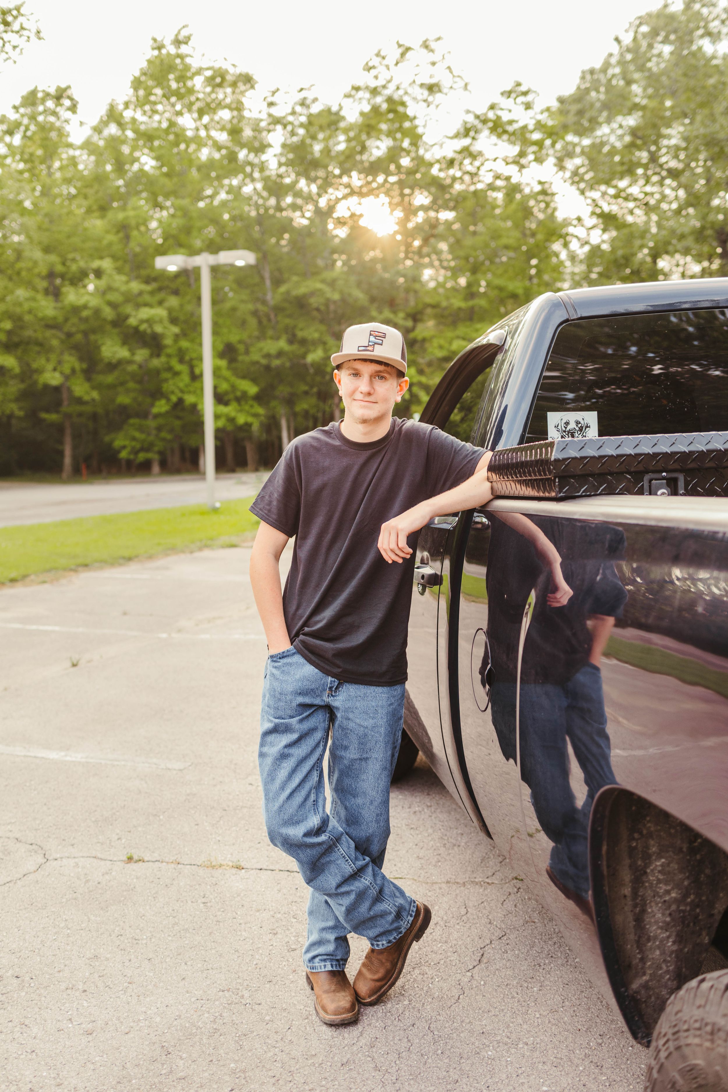 Casual photo of person leaning against black pickup truck in parking lot.