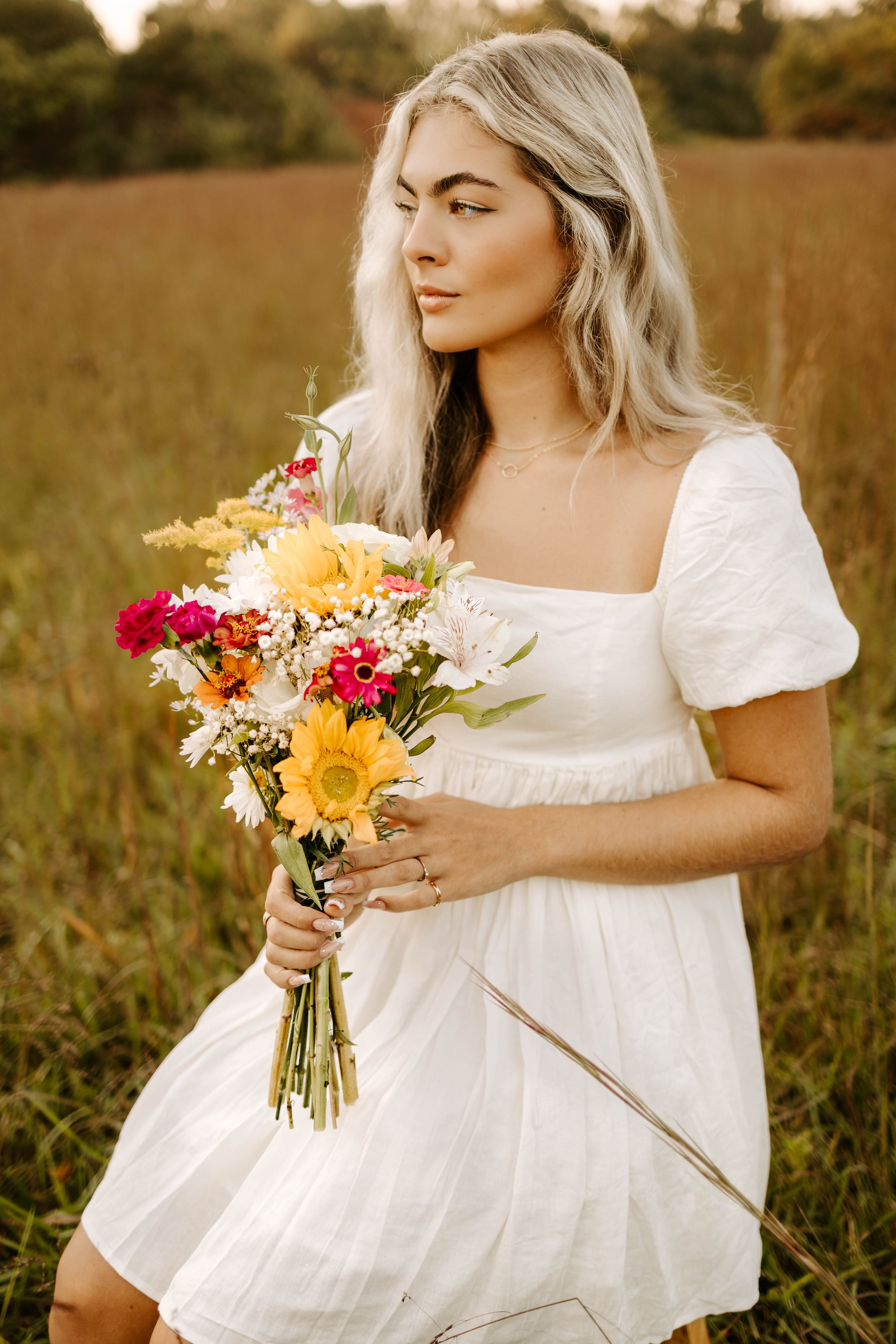 A white sundress contrasts beautifully with vibrant sunflowers and wildflowers in a golden meadow.
