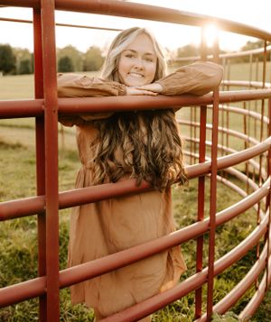 Portrait at sunset through red metal fence with warm golden lighting.