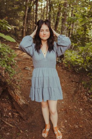 Person in flowy blue dress poses on forest trail wearing sandals.
