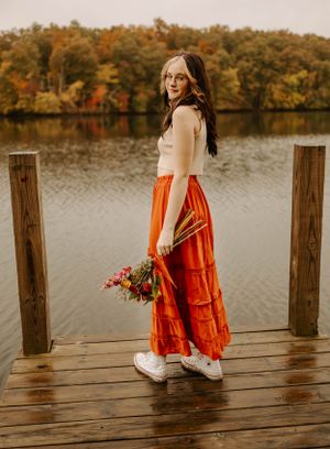 A stylish autumn portrait on a dock featuring a flowing orange skirt, white top and colorful bouquet.