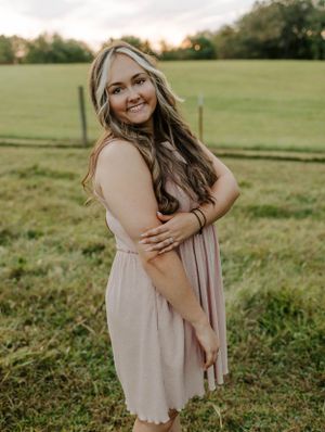 Woman in blush pink dress poses in a grassy field at sunset.