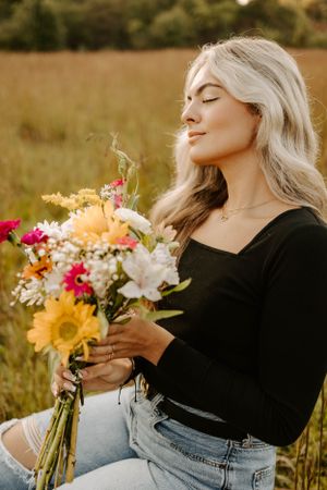 Woman holding colorful wildflower bouquet in sunlit meadow.
