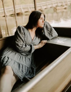 Artistic portrait in grey dress sitting in boat with dreamy expression.