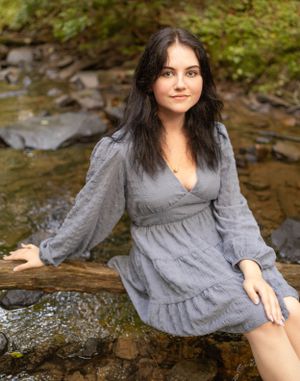 Portrait in grey dress sitting among creek rocks with water flowing.
