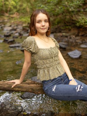 Portrait at creek with person sitting on log wearing peasant top and jeans.