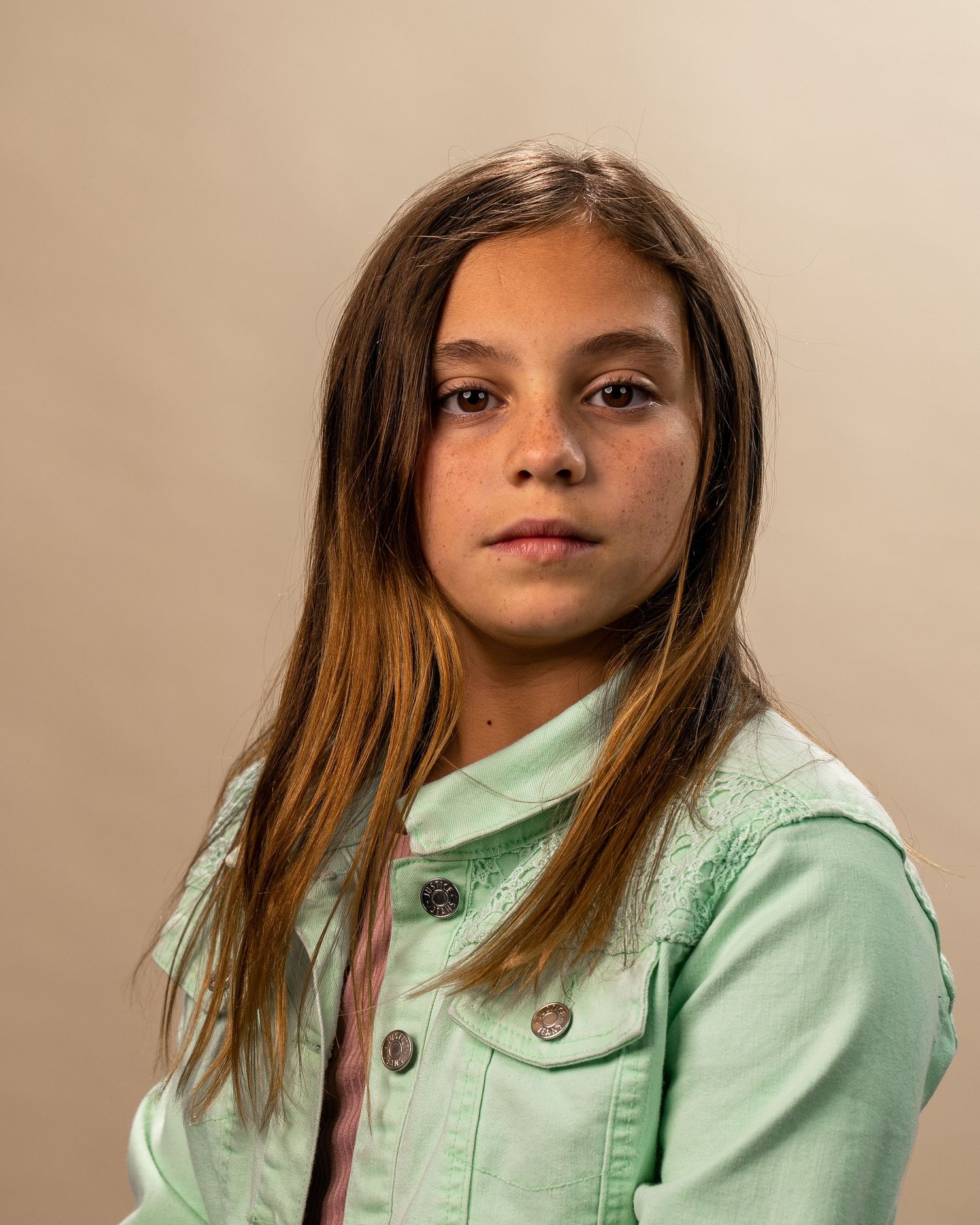 Portrait of a young person in a mint green jacket posing against a beige background.