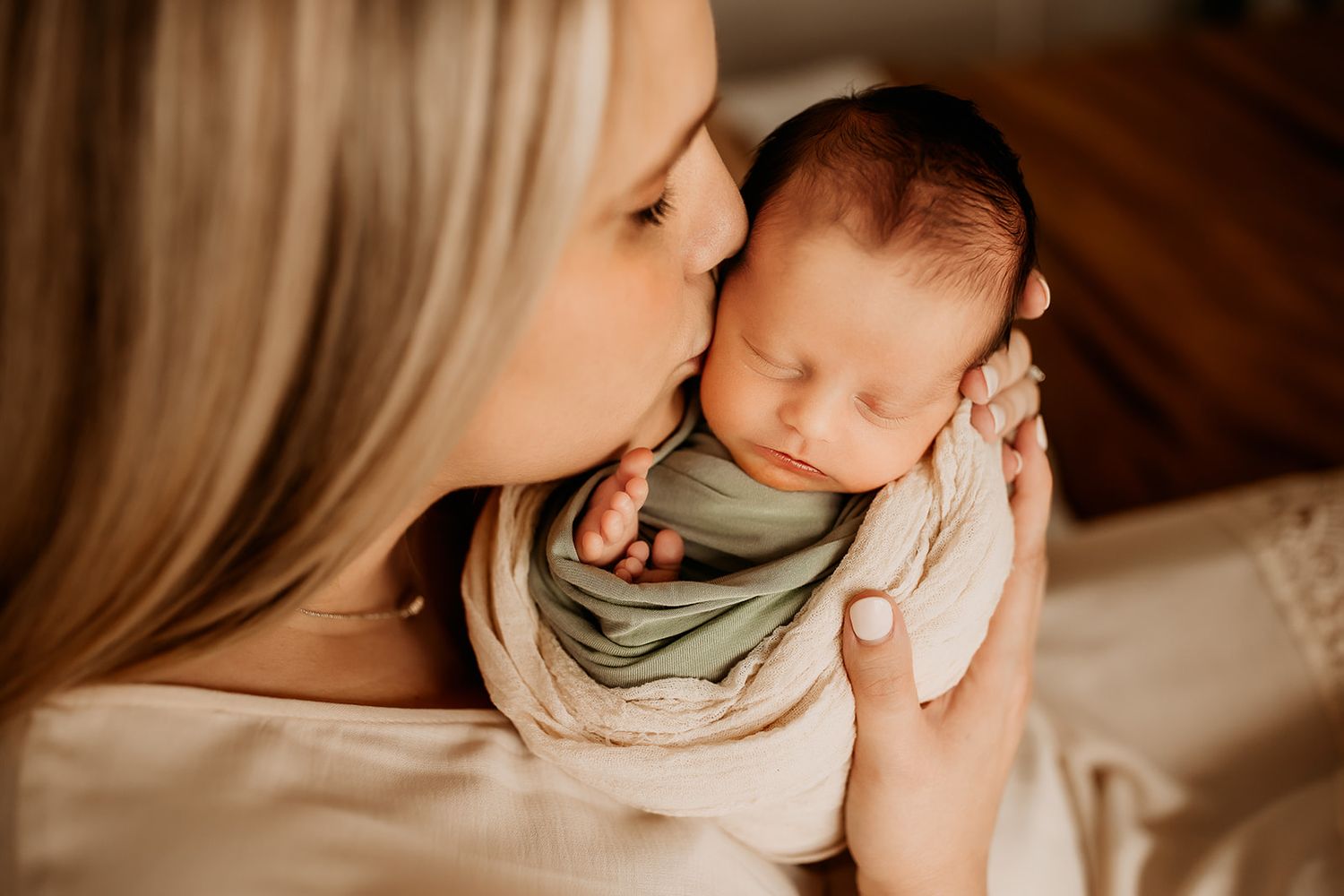 A mother holds her baby boy close and kisses his temple.