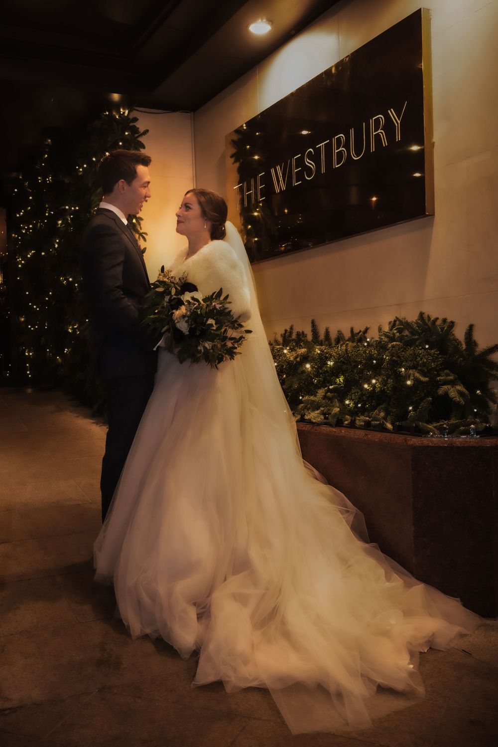 Bride and groom share a romantic moment outside The Westbury hotel, surrounded by festive Christmas trees and warm lights.