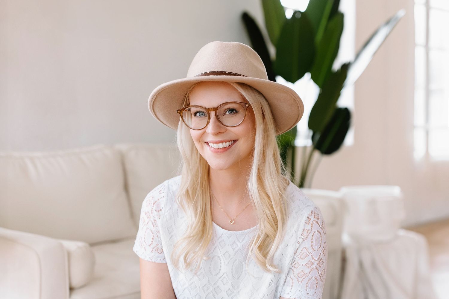 Headshot of Jackie, smiling, wearing round glasses with brown rims, blonde hair, beige hat