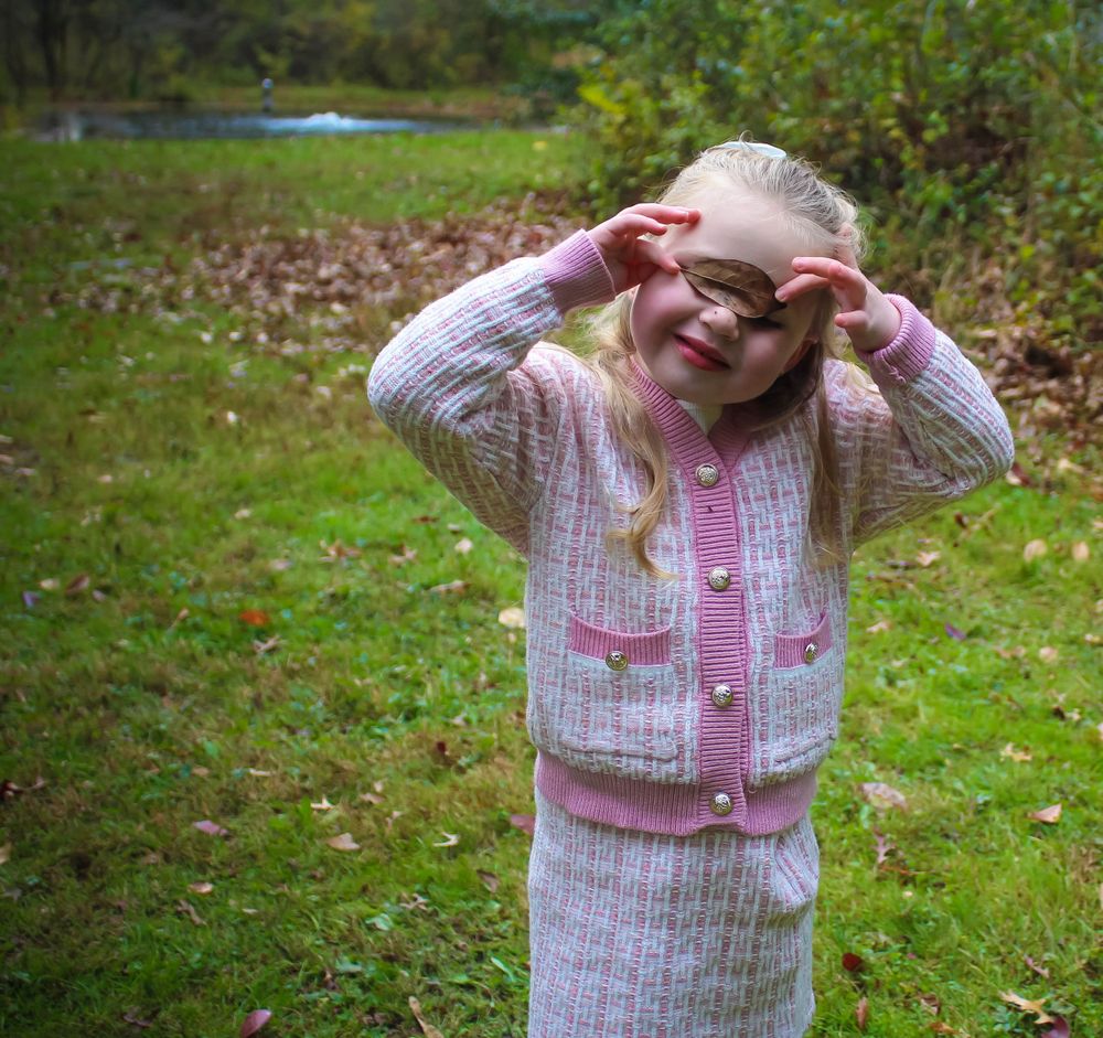 Young child in pink knit outfit playing and making silly faces in backyard.
