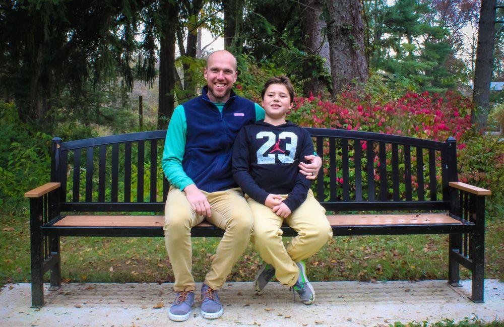 Two people sitting together on park bench surrounded by fall foliage.