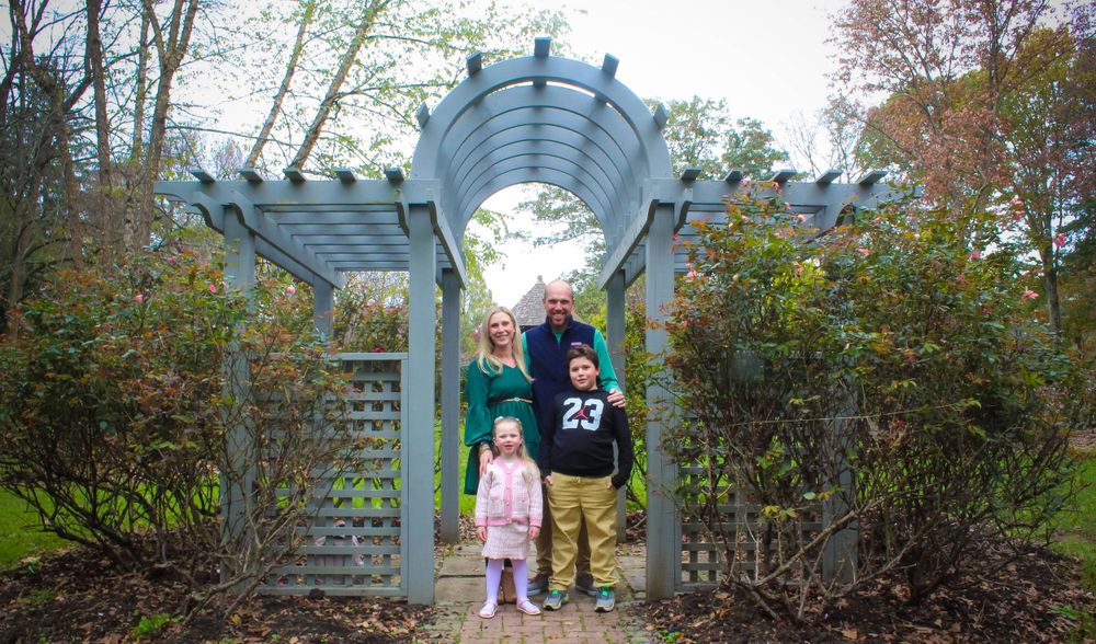 Two people standing under decorative garden archway surrounded by autumn foliage.
