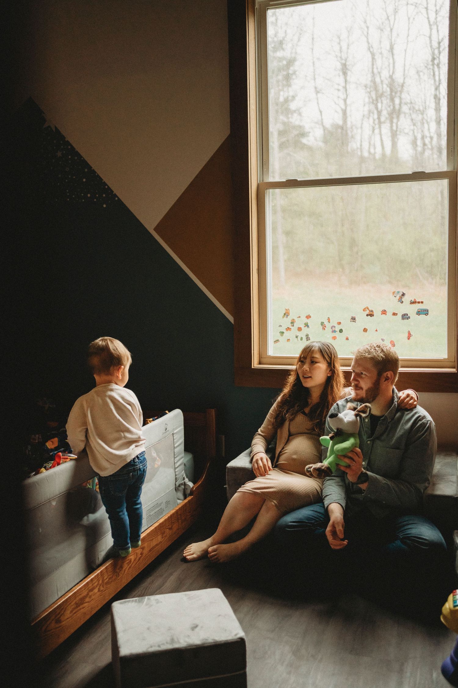A family shares a moment together in a cozy room with a large window and dark accent wall.