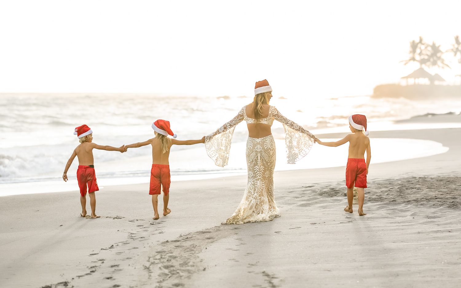 Beach celebration with people in festive attire holding hands along shoreline at sunset.