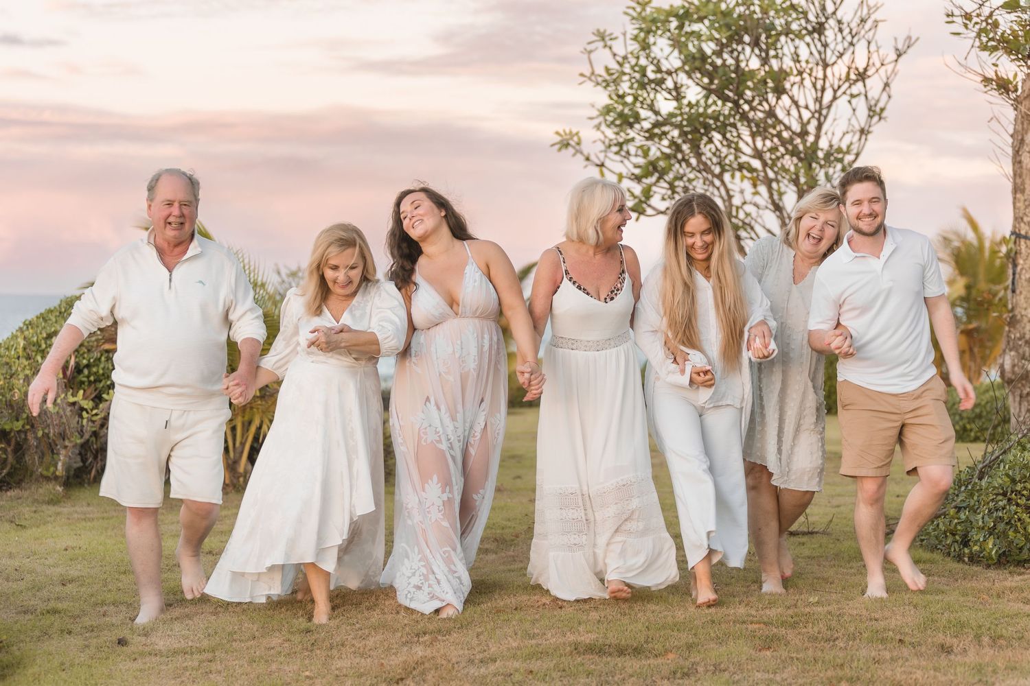 Group dressed in white and beige casual attire poses together during sunset.